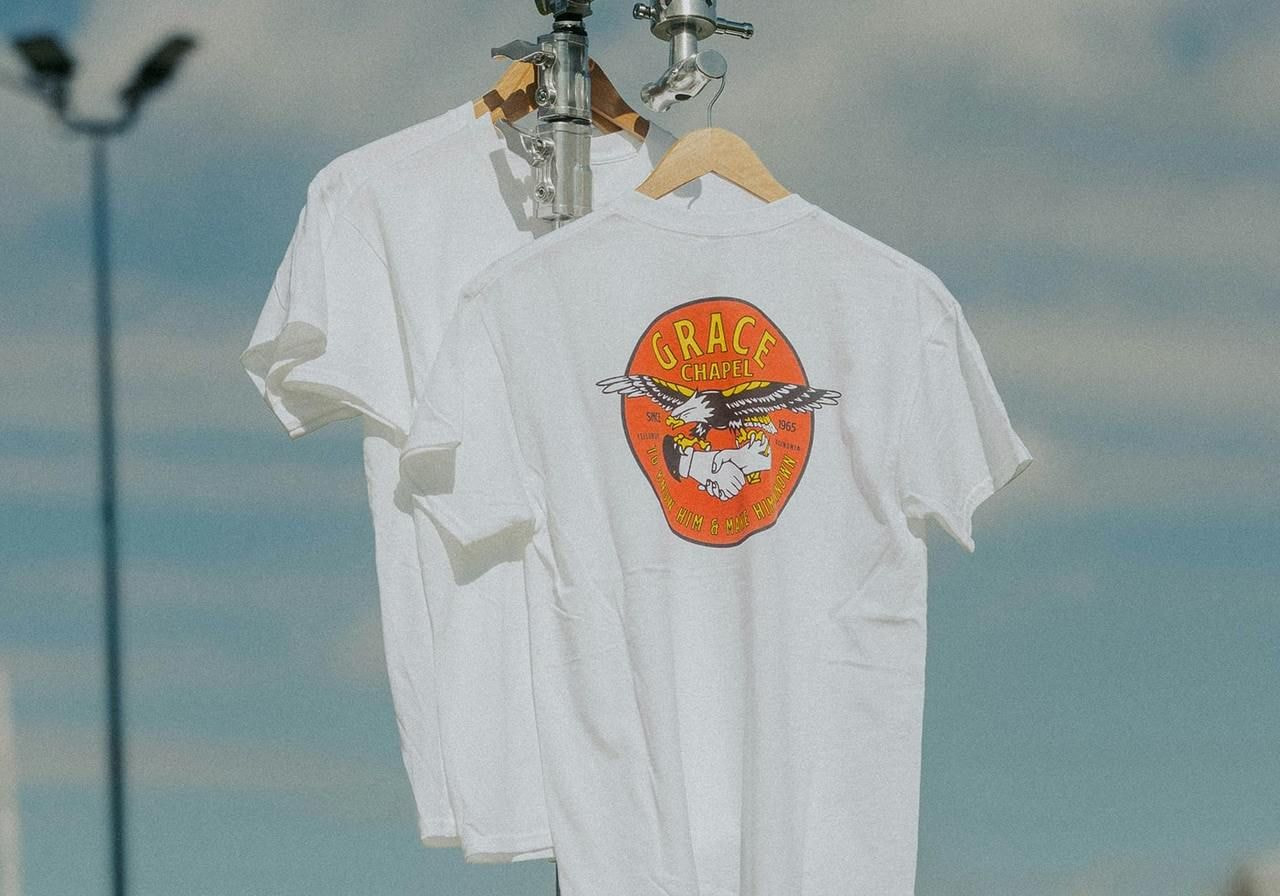 A white t-shirt featuring a bird design, hanging on a clothesline against a clear sky.
